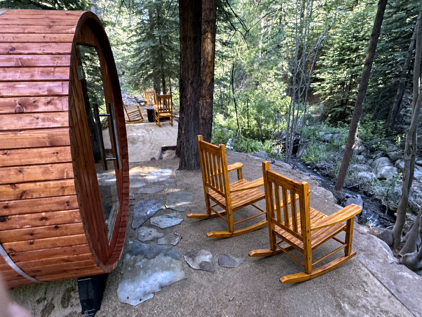 Rocking chairs beside the barrel sauna with the creek and pines alongside