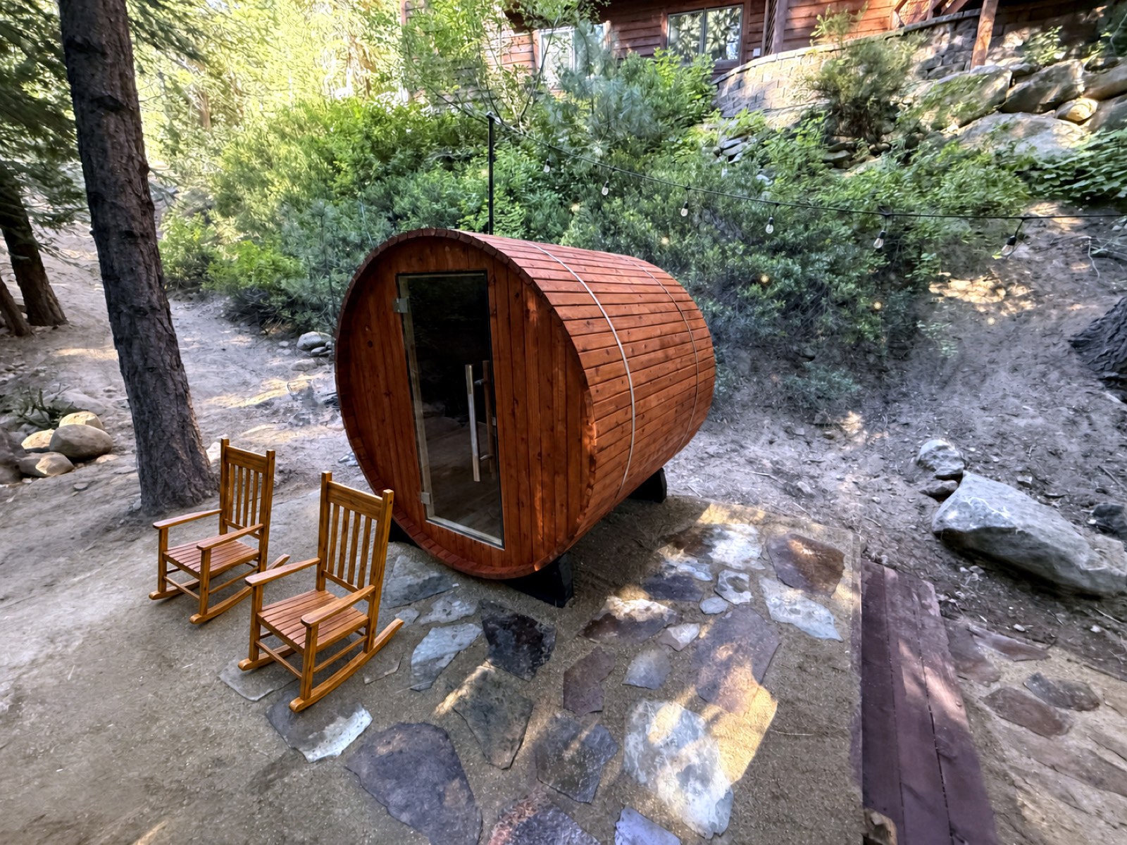 Cedar barrel sauna and rocking chairs on the flagstone terrace by day, set among the pines